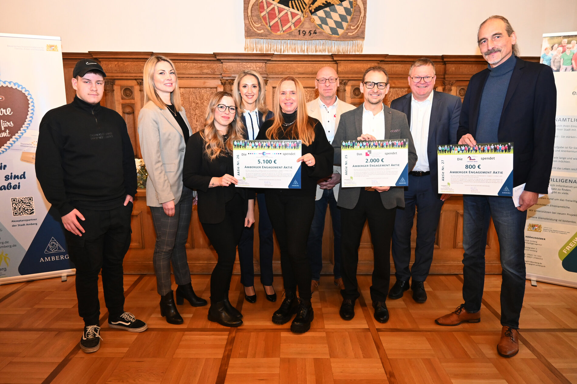 Das Bild zeigt die Übergabe der Engagement-Aktie als Dankeschön für die Unterstützung mit Dennis Ullmann (Freiwilligenagentur), Nadine Murshel (Freiwilligenagentur), Nadine Lutter (Schmidt und Wifling GmbH), Elisabeth Triller (Leiterin Freiwilligenagentur), Regina Wifling (Geschäftsführerin Schmidt und Wifling GmbH), Torsten Wolf (Wohnungsbau Siedlungswerk Werkvolk eG), Wolfgang Erb (Vorstand Wohnungsbau Siedlungswerk Werkvolk eG), Michael Cerny (Oberbürgermeister), Martin Malitzke (Geschäftsführer Stadtwerke Amberg GmbH). 