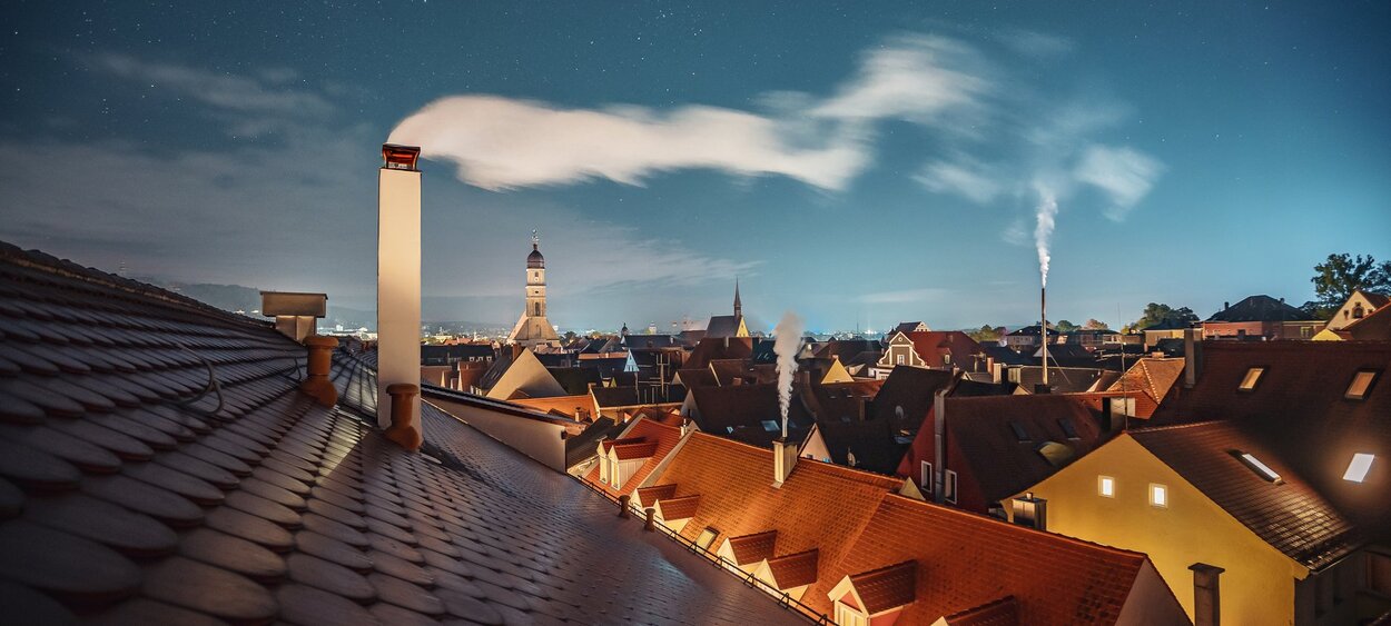 Das Foto zeigt Hausdächer mit rauchenden Kaminen in Amberg bei Nacht.